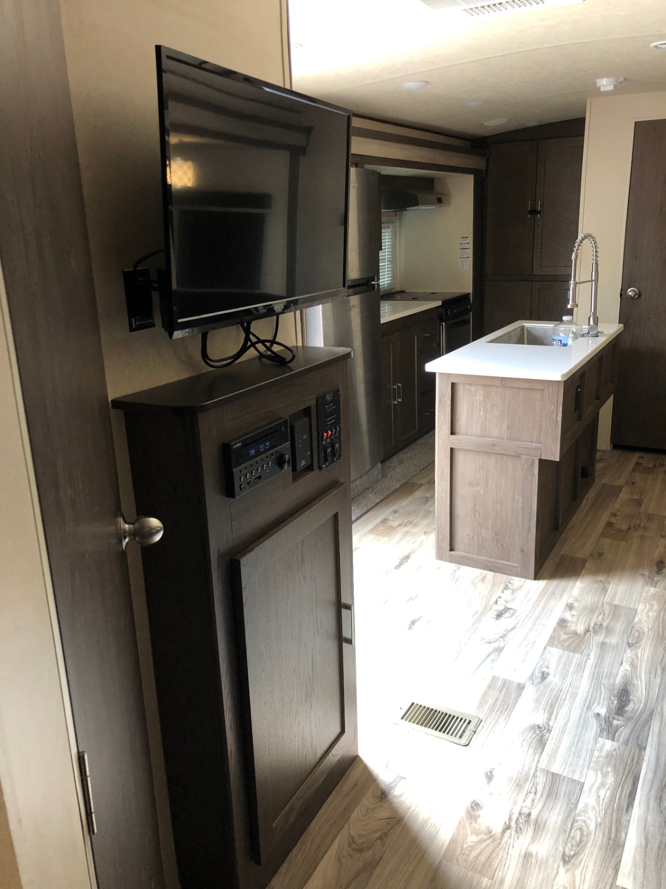 View from the bedroom into the 2018 Heritage Glen LTZ 312QBUD kitchen with island and stainless refrigerator