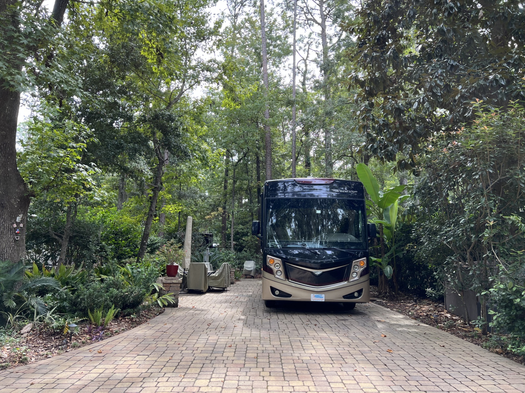 2016 Fleetwood Excursion 35E parked on a brick pad surrounded by a lush garden and tropical foliage