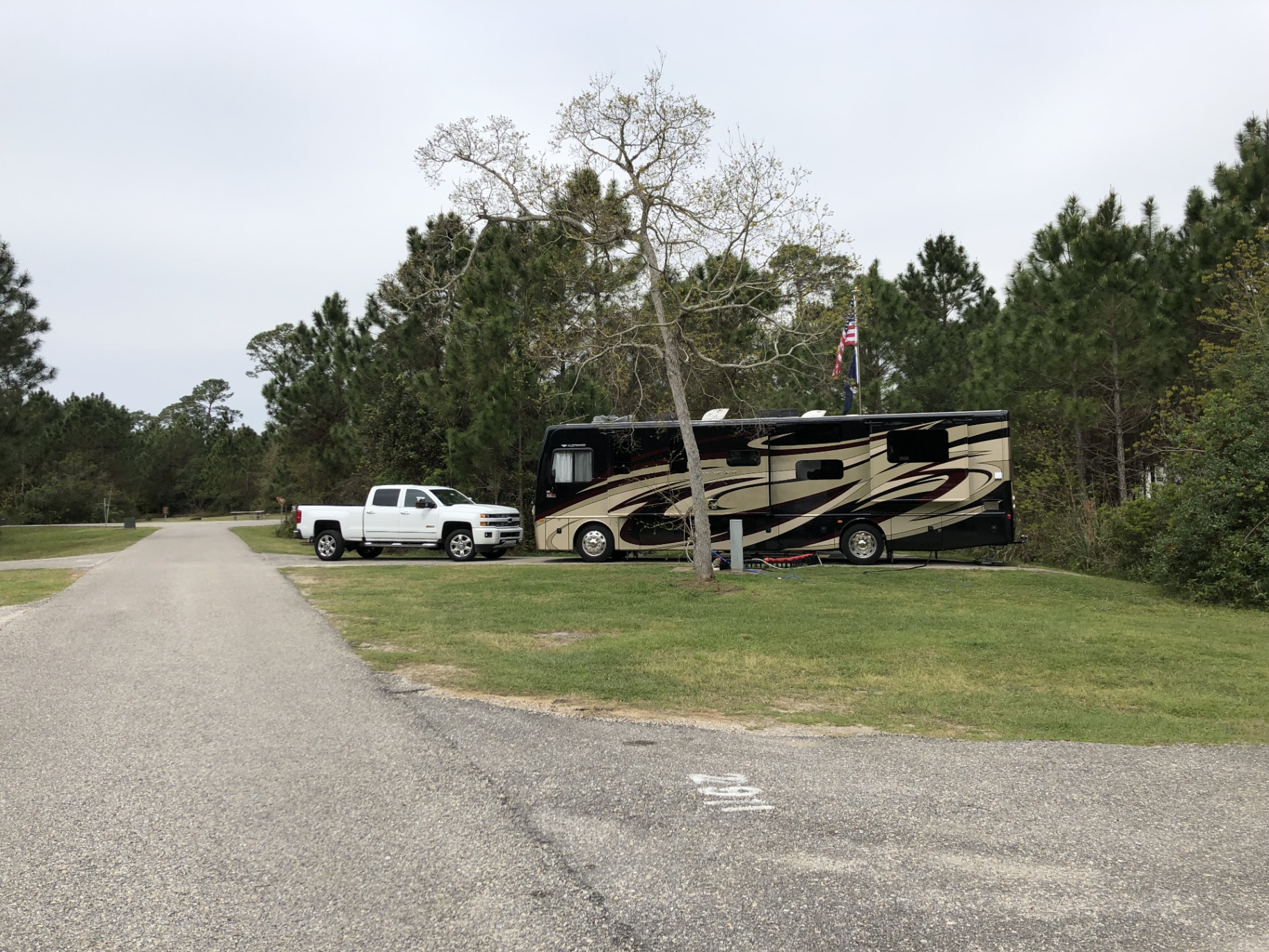 2016 Fleetwood Excursion 35E motorhome and Chevy Silverado parked at a grassy campsite among pine trees