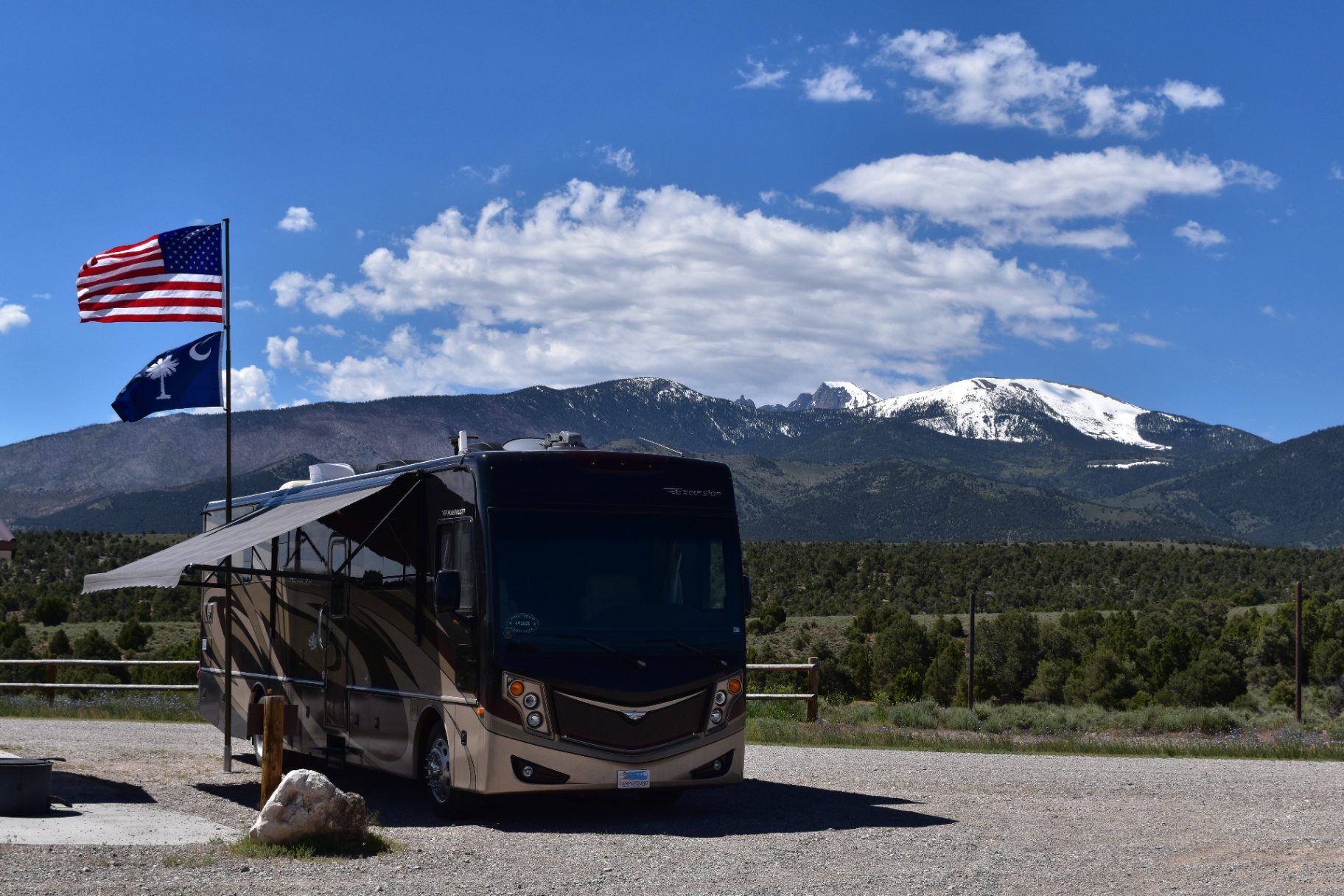2016 Fleetwood Excursion 35E Class A motorhome at a Rocky Mountain campsite with snowcapped peaks and flags flying