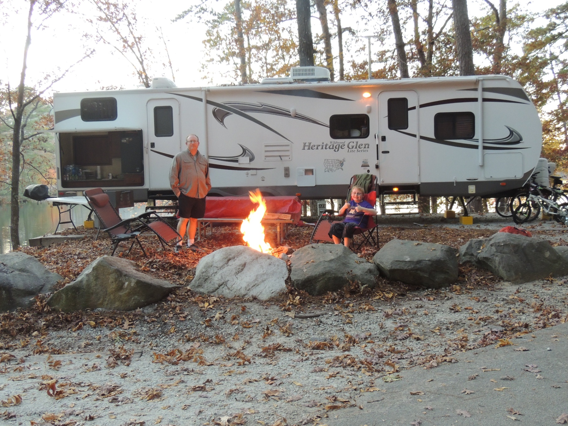 Father and son sitting at the campfire at dusk in front of the 2013 Forest River Heritage Glen 312QBUD travel trailer