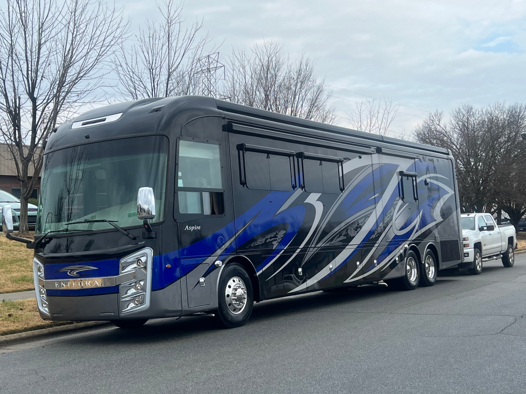 Driver-side exterior view of the 2021 Entegra Aspire 44W parked with a white pickup truck behind it