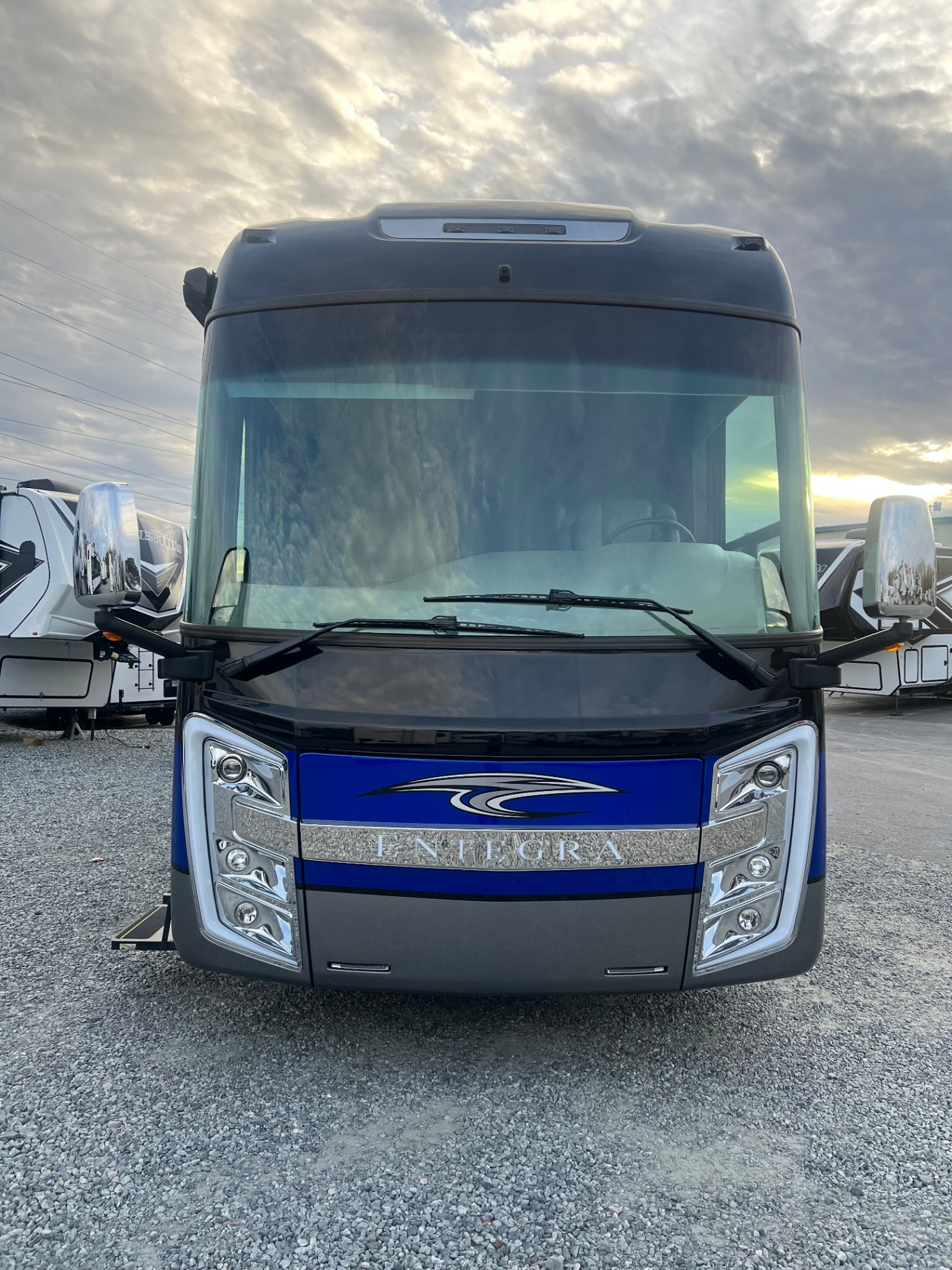 Front view of the 2021 Entegra Aspire 44W motorhome at the dealership under a dramatic cloud-filled sky