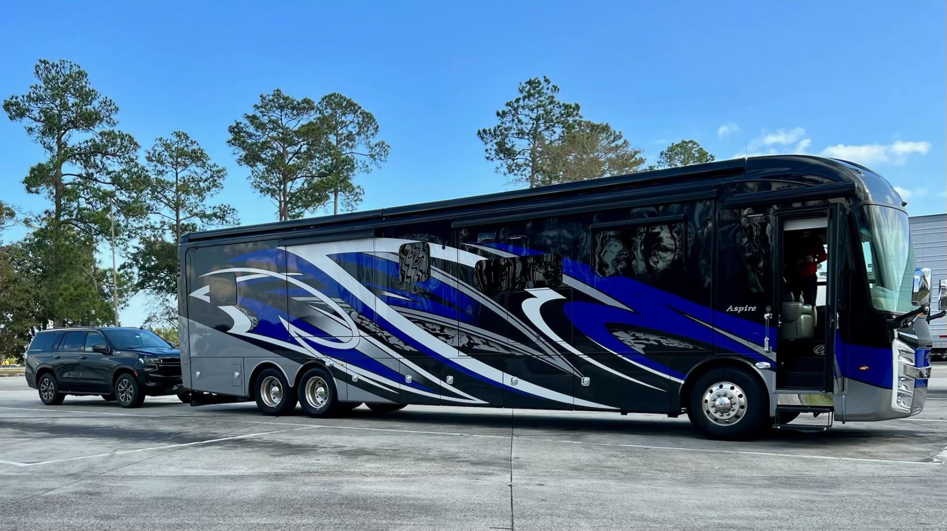 2021 Entegra Aspire 44W towing a black SUV at a roadside stop under a blue sky