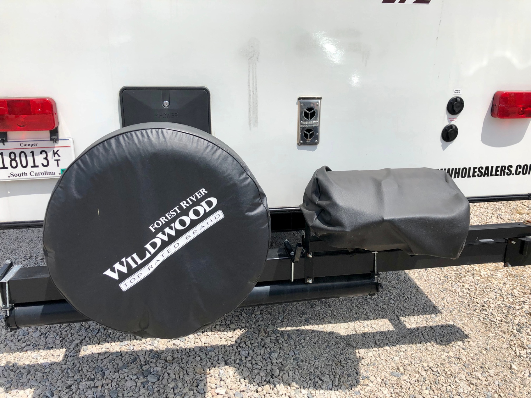 Rear exterior of the 2018 Heritage Glen LTZ 312QBUD with spare tire cover, outdoor shower, and camper tag