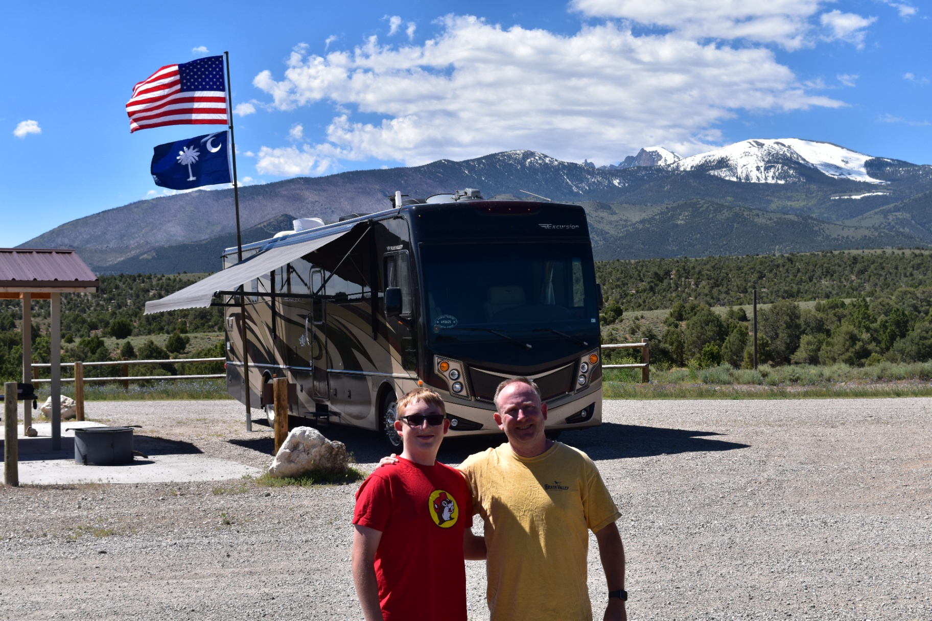Father and son standing in front of the 2016 Fleetwood Excursion 35E with snowcapped Rocky Mountains in the background