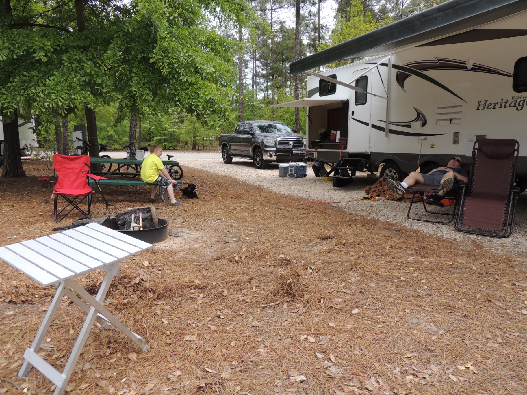 Evening campfire beside the Heritage Glen 312QBUD with the exterior outdoor kitchen hatch open