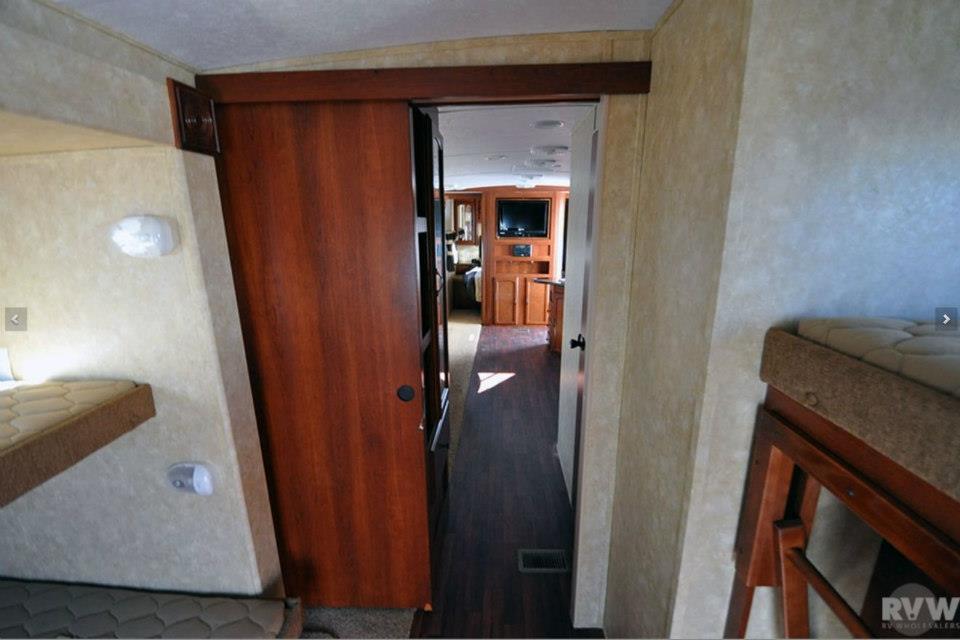 Interior hallway of the Heritage Glen 312QBUD looking through the sliding wood door toward the living room and entertainment center