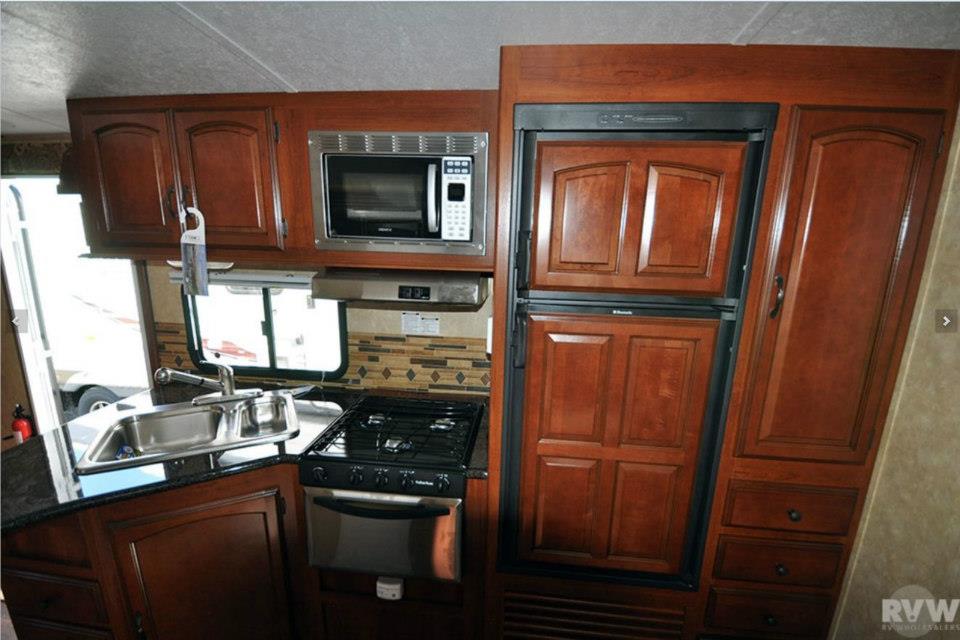 Heritage Glen interior kitchen with three-burner gas stove, overhead microwave, stainless sink, and double-door refrigerator