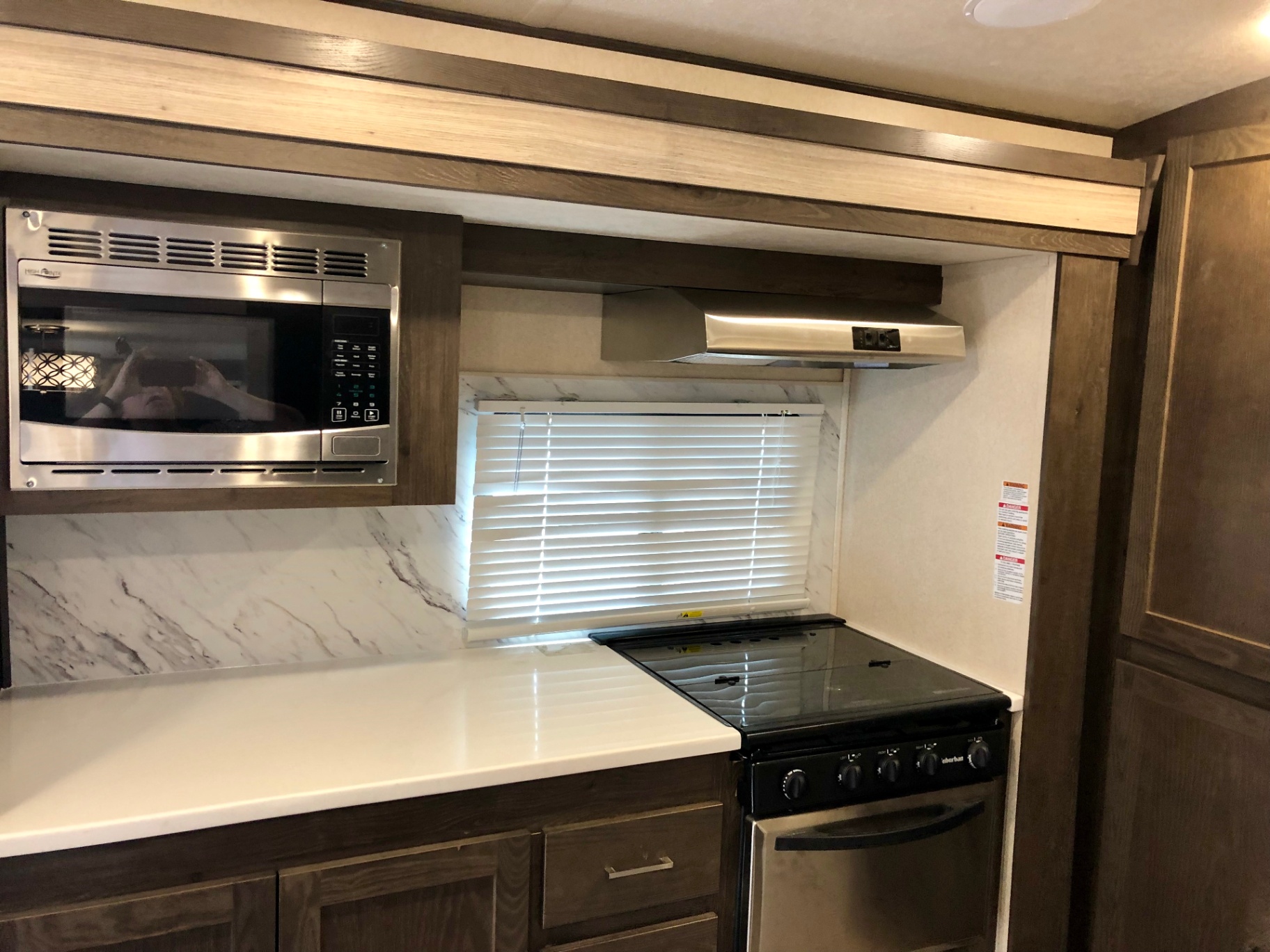 2018 Heritage Glen LTZ 312QBUD kitchen with gas range, microwave, vent hood, and solid-surface style counters