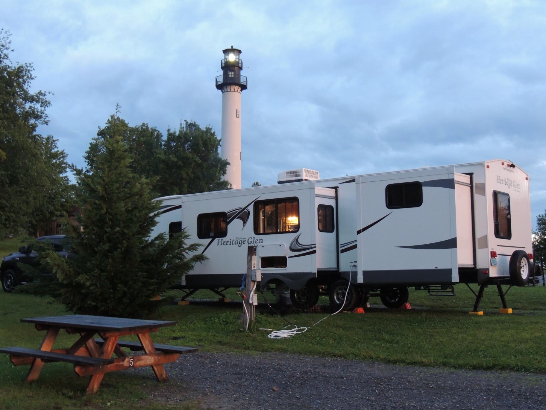Heritage Glen travel trailer parked beside a coastal lighthouse at dusk