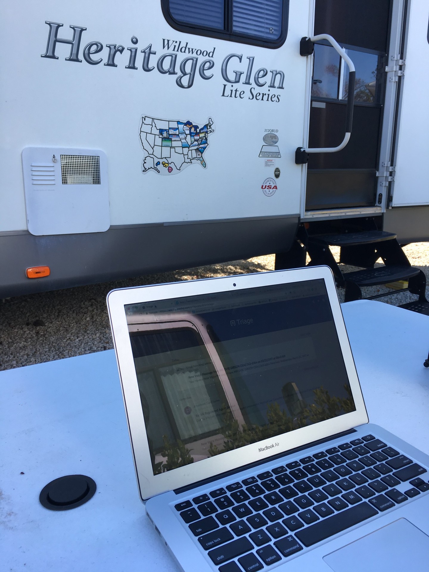 MacBook open on a picnic table outside a Wildwood Heritage Glen travel trailer — working from the road in 2017